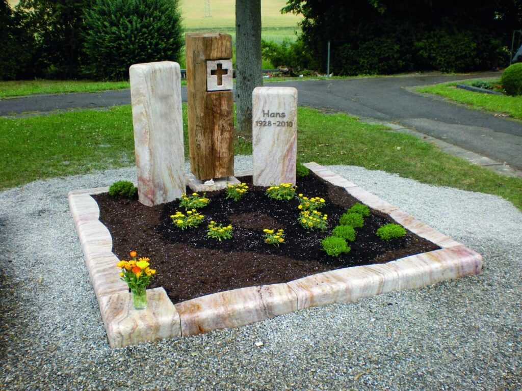 Grabsteine: Grab mit Inschrift "Hans 1928-2010", Kreuz und gelben Blumen. Steinmetz Meisterbetrieb