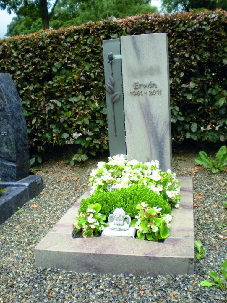 Grabstein mit der Inschrift "Erwin 1941-2011", geschmückt mit Blumen und einem Engel. Grabsteine. Steinmetz Meisterbetrieb