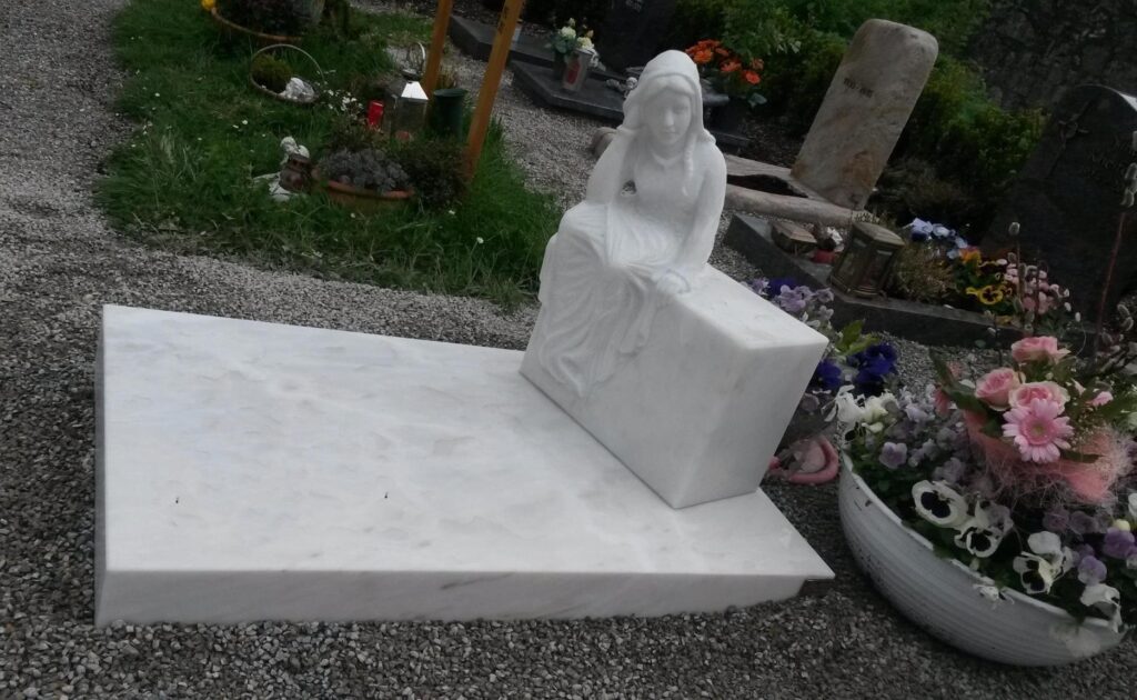 Weißer Grabstein mit einer Skulptur einer sitzenden Frau. Grabsteine. Steinmetz Meisterbetrieb