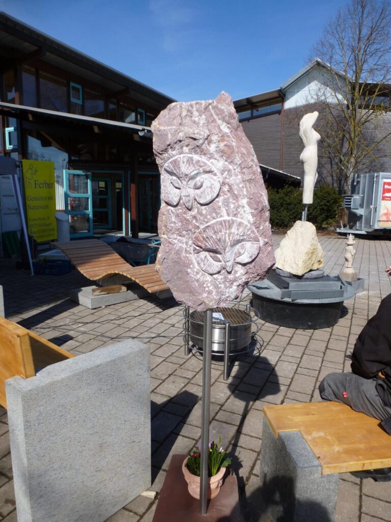 Steinskulptur mit zwei Eulen, "Gestalten mit Naturstein" im Hintergrund. Steinmetz Meisterbetrieb