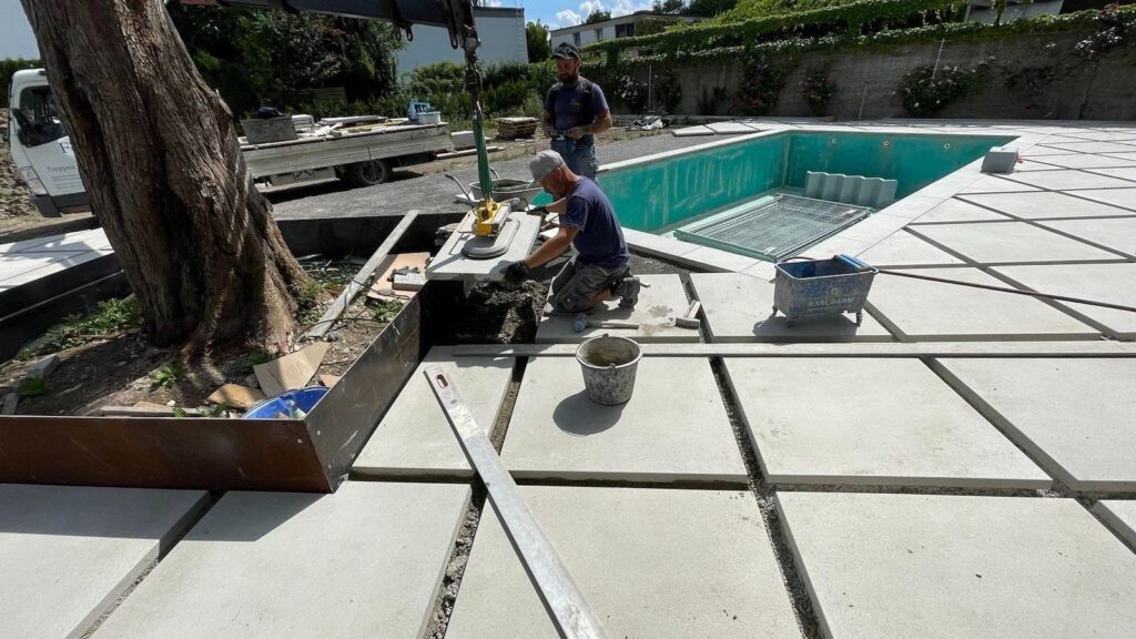 Landschaftsgärtner verlegen Platten um einen Pool. Meisterbetrieb im Gartenbau. Steinmetz Meisterbetrieb