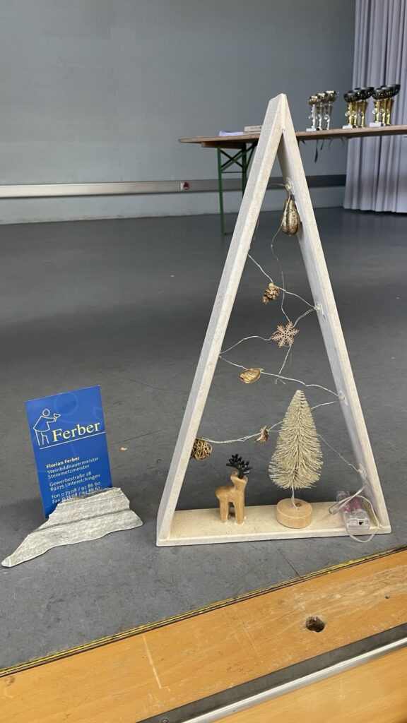 Steindekoration: Dreieckige Holzdeko mit Hirsch, Baum und Lichtern. Visitenkarte von Florian Ferber. Steinmetz Meisterbetrieb